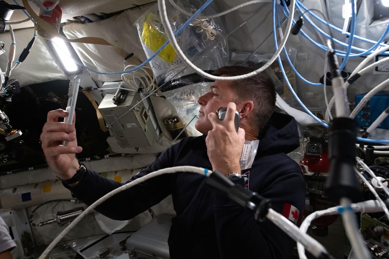 Astronaut shaving inside spacecraft using electric razor and mirror phone app.